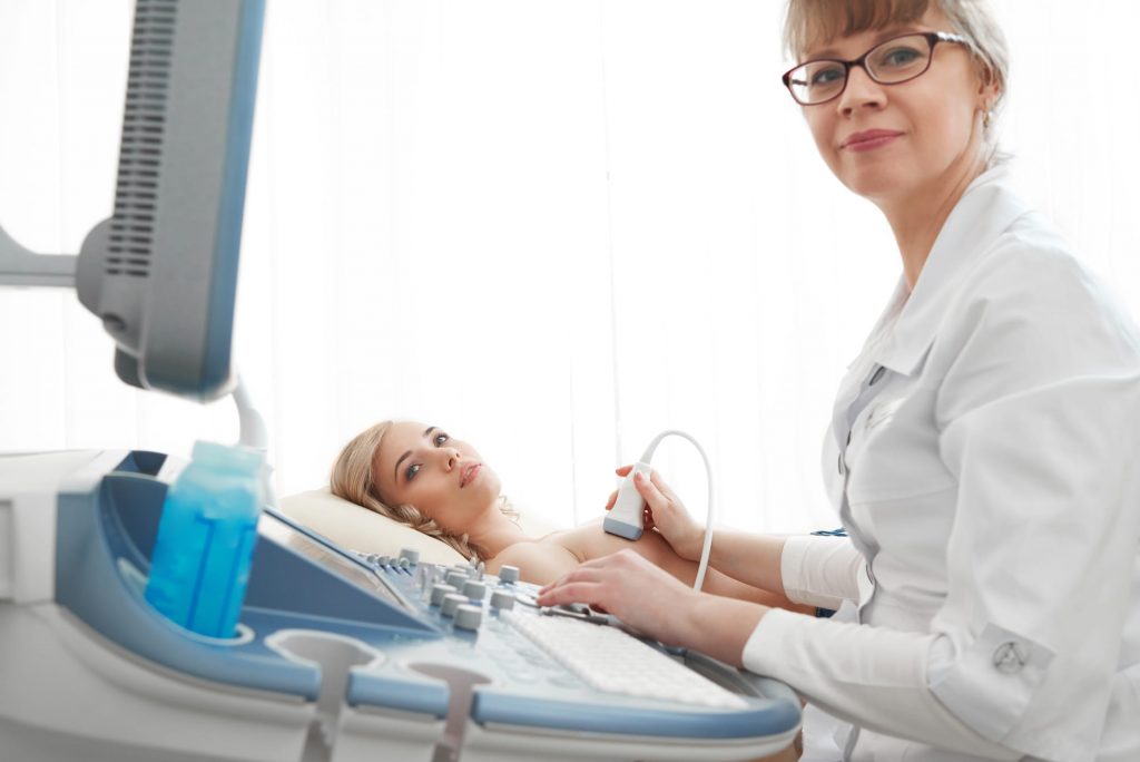 Eine junge Ärztin macht bei einer Patientin eine Ultraschalluntersuchung an der Brust